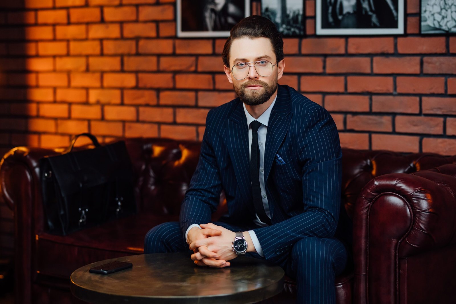 Confident businessman in stylish suit sitting on leather sofa in modern office studio